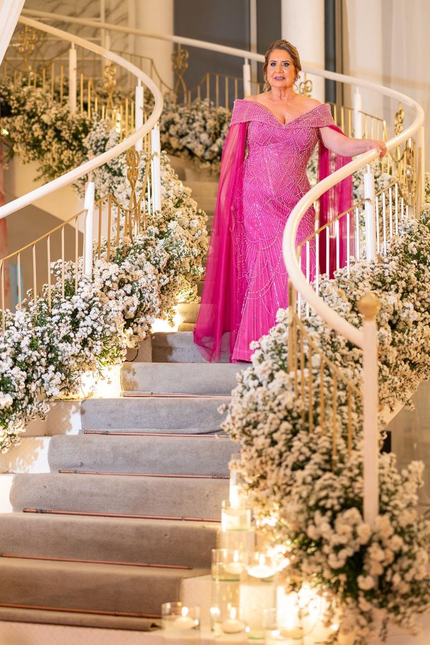 Aniversariante em vestido rosa descendo escadaria decorada com flores brancas