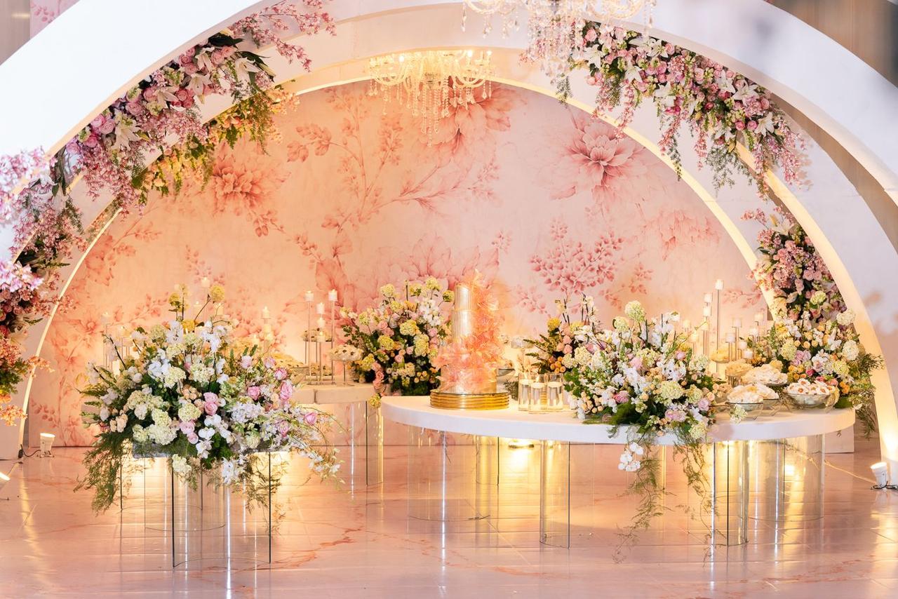 Mesa do bolo com arranjos de flores e arcos florais
